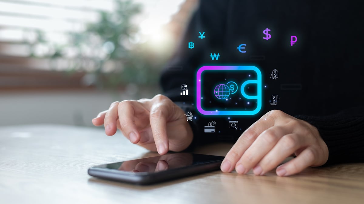 Hands using a smartphone with a digital wallet icon and global currency symbols