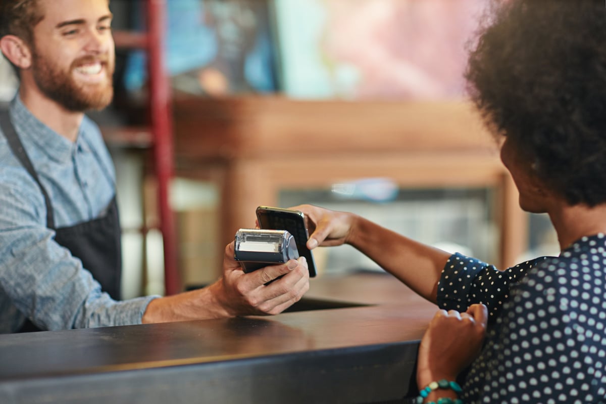 Barista taking a smartphone payment from a customer at a cafe counter